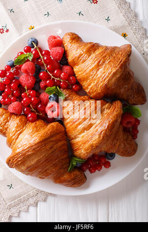 Golden croissants with fresh summer berries close-up on a plate. Vertical view from above Stock Photo