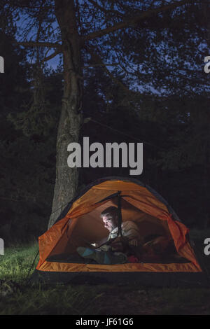 Man watching his smartphone in a tent. Stock Photo