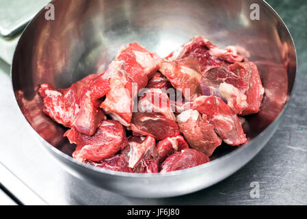 Pieces of fresh raw red meat in a stainless steel bowl ready for cooking in a recipe in a close up overhead view Stock Photo