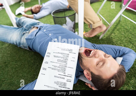 Young businessmen sleeping on green grass carpet at modern office, business teamwork Stock Photo
