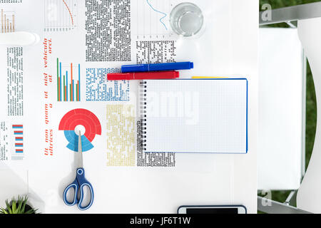 Top view of blank notebook, business charts and office supplies at workplace Stock Photo