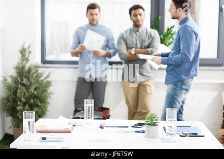 Close-up view of documents and business charts on desk and businessmen standing behind, business teamwork concept Stock Photo