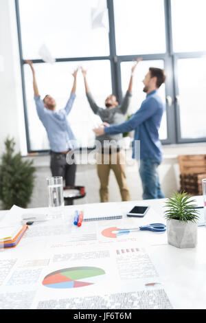 Close-up view of documents and business charts on desk and businessmen throwing papers behind, business teamwork concept Stock Photo