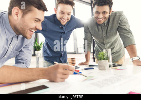 Three young businessmen leaning at table and working at project together, business teamwork concept Stock Photo