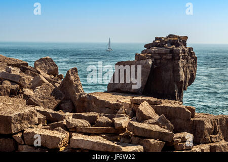 Seascape depicting the Pulpit Rock from the Quarries pathway, a passing sail boat surrounded by blue skies and calm seas on a beautiful summers day. Stock Photo