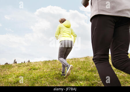 Unrecognizable senior couple running outside on green hills. Stock Photo