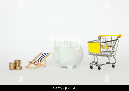 A stack of coins with a deck chair, piggy bank and a shopping cart on white background, copyspace Stock Photo