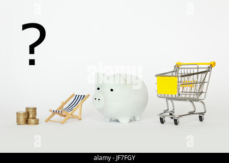 A question mark above a stack of coins, a deck chair, piggy bank and a shopping cart on white background, symbolic for spending income, earnings or re Stock Photo