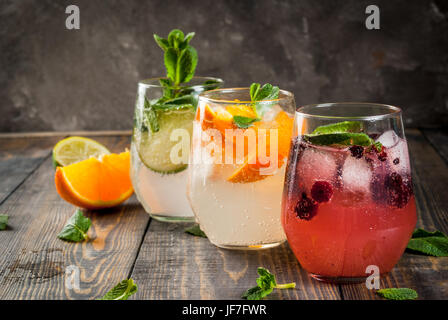 Selection of three kinds of gin tonic: with blackberries, with orange, with lime and mint leaves. In glasses on a rustic wooden background. Copy space Stock Photo