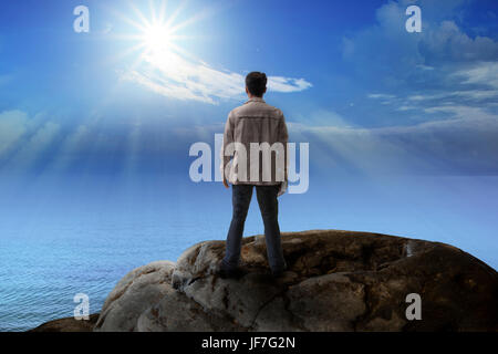 young man standing on rock mountain and looking to the sun for multipurpose Stock Photo
