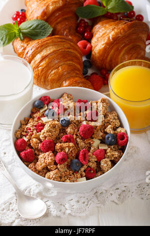 Muesli with dried berries and white chocolate, croissants, milk and orange juice close-up on the table. vertical Stock Photo