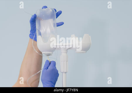 Doctor's hands and infusion drip in hospital on blurred background Stock Photo
