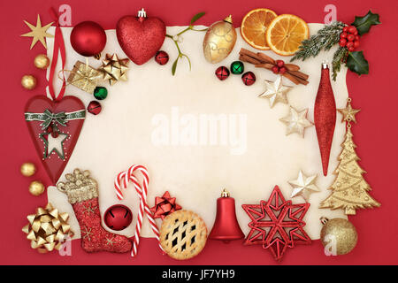 Abstract christmas border with bauble decorations, holly, mistletoe, fir, dried orange and mince pie on parchment paper and red background. Stock Photo