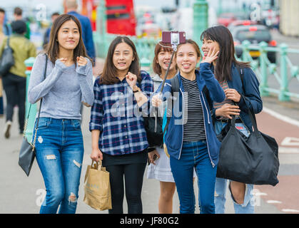 Taking a selfie. Group of Asian friends taking a group selfie using a smartphone on a selfie stick. Stock Photo
