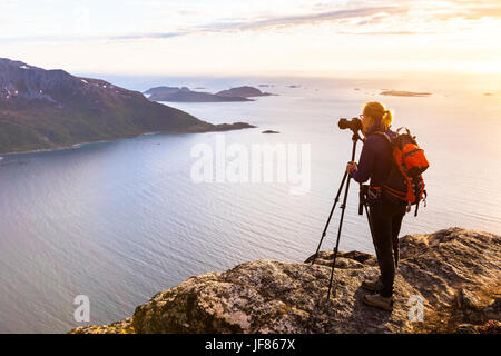 Woman photographer taking photo of a beautiful fjord in Norway at golden hour with DSLR camera and tripod Stock Photo