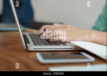 Asian male hand typing on laptop computer keyboard while working in coffee shop on workday. Freelancer lifestyle and activity concept