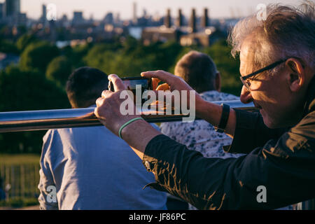 Man leaning his smartphone on the metal raining, stabilising to take photo on his smartphone Stock Photo