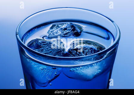 Deep blue colored drink with ice close up. On abstract blue background. Stock Photo
