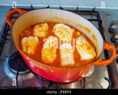 A fish stew cooking in an orange casserole dish, when the stew is ready the fish steaks are placed on top to cook for a few minutes in the steam Stock Photo