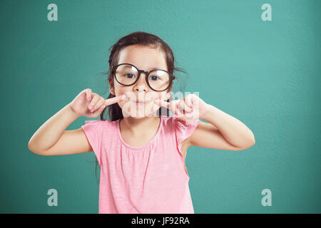 Happy little Asian girl with glasses smiling isolated on vintage mint green background . Stock Photo