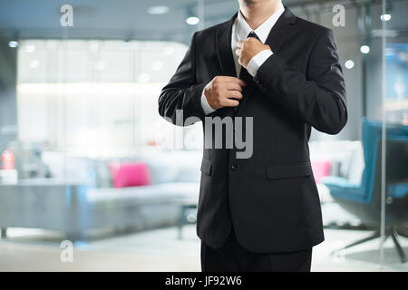 Smart businessman in black suit with adjust the tie pose . Stock Photo