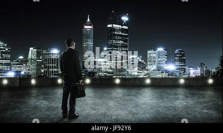 Businessman looking and thinking at roof top with modern city skyline background , night scene . Stock Photo