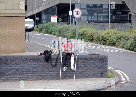 boy with broken leg in cast sitting on wall outside hospital waiting for taxi or texting calling for a cab Stock Photo