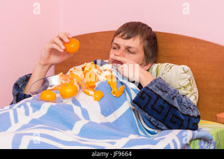 A man who lies in bed sick of mandarins Stock Photo