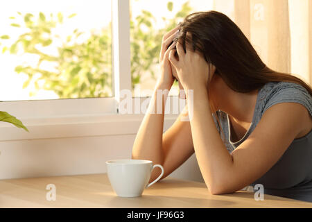 Single sad woman covering face sitting in a table at home Stock Photo