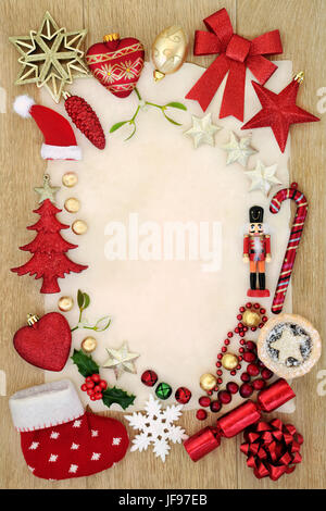 Christmas background border with bauble decorations, mince pie, foil wrapped chocolates, holly and  mistletoe on parchment paper oak wood. Stock Photo