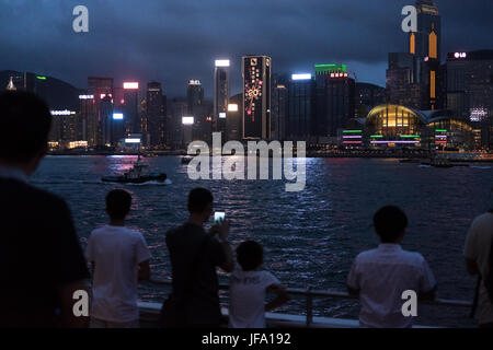 Hong Kong. 24th June, 2017. People stand in front of Victoria Harbour with a view of decorated buiding celebrating the 20th anniversary of the Hong Kong handover from Britain to China on Saturday June 24, 2017. Credit: Sun Yeung/Pacific Press/Alamy Live News Stock Photo