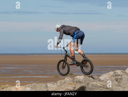 Teenager performing cycling tricks at Hoylake, Wirral.  Uk Weather. Sunny day on the west coast as beachgoers return to the sands of the resort after days of overcast and fresher weather. Today is to continue dry with some pleasantly warm sunny spells for most through the middle of the day. Stock Photo