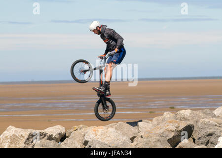 Teenager performing cycling tricks at Hoylake, Wirral.  UK Weather. Sunny day on the west coast as beachgoers return to the sands of the resort after days of overcast and fresher weather. Today is to continue dry with some pleasantly warm sunny spells for most through the middle of the day. Stock Photo