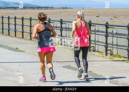 Female summer joggers in Hoylake, Wirral.  Uk Weather. Sunny day on the west coast as beachgoers return to the sands of the resort after days of overcast and fresher weather. Today is to continue dry with some pleasantly warm sunny spells for most through the middle of the day. Stock Photo