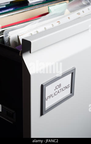 An open filing drawer, labeled 'Job Applications' and filled messily with hanging files, folders, plastic wallets and papers.  Portrait orientation. Stock Photo