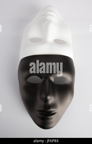 Black and white masks joined on white reflective background. Vertical image, top view. Anonymity concept.