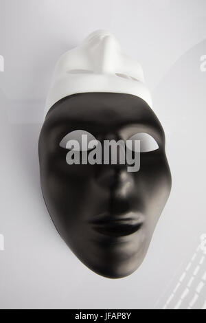 Black and white masks joined on white reflective background. Wide angle, vertical image, top view.