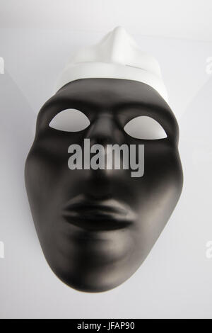 Black and white masks joined on white reflective background. Wide angle, vertical image, top view.