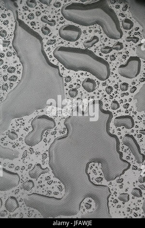 Very irregular patches of water adhering to a gray plastic table cloth after a rain, creating an unusual pattern on an overcast day. Stock Photo