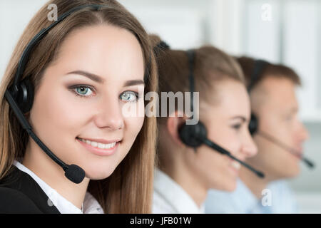 Portrait of call center worker accompanied by her team. Smiling customer support operator at work. Help and support concept Stock Photo