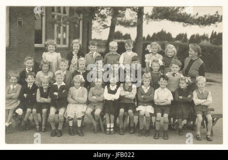 Postcard depicting a class of school children with their teacher outside posing in summer uniform, In the front row is a girl in calipers, probably a victim of polio, circa early 1950's, U.K. Stock Photo