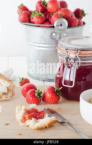 A farmhouse kitchen table scene of freshly made strawberry jam in storage jar with a tin pail of strawberries in the background and bread and strawber Stock Photo