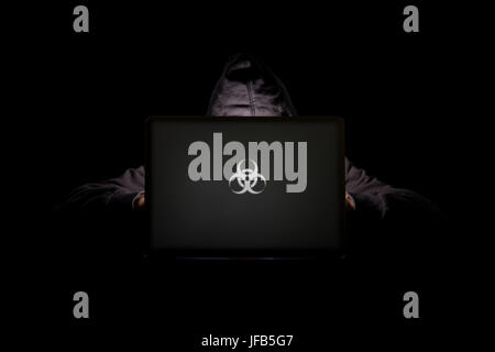 A person in a dark room using a laptop with a biohazard logo, internet phishing, hacking, data security threats, data breach, cyber security concept Stock Photo