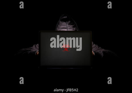 A person in a dark room using a laptop with a red biohazard logo, internet phishing, hacking, and personal information theft, data security threats Stock Photo