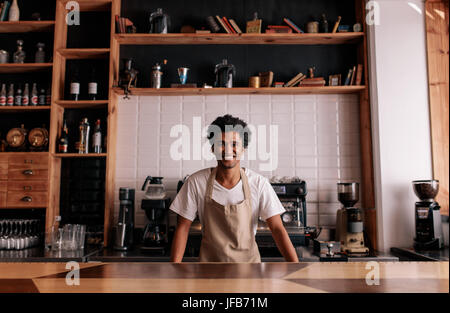 Portrait of professional barista standing at cafe counter. African man in apron looking at camera and smiling. Stock Photo
