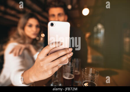 Close up of couple sitting in the bar and taking a selfie with smart phone. Focus on mobile phone in hand of woman.