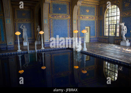The Roman Pool at Hearst Castle, styled after an ancient Roman bath, is tiled with mosaic patterns in blue and gold, lit with ornate lighting, and surrounded by sculptures. Stock Photo