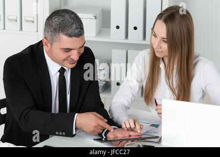 Young beautiful business woman consulting with her male colleague showing something on tablet PC. Partners discussing documents and ideas Stock Photo