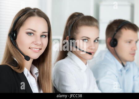 Portrait of call center worker accompanied by her team. Smiling customer support operator at work. Help and support concept Stock Photo
