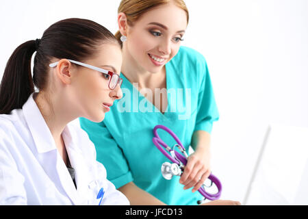 Two beautiful female medicine doctors looking at laptop monitor and smiling. Medical and healthcare concept Stock Photo